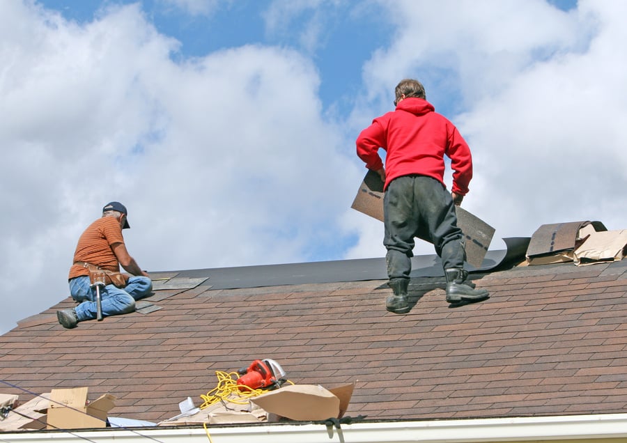 Two men replacing shingles on a house roof